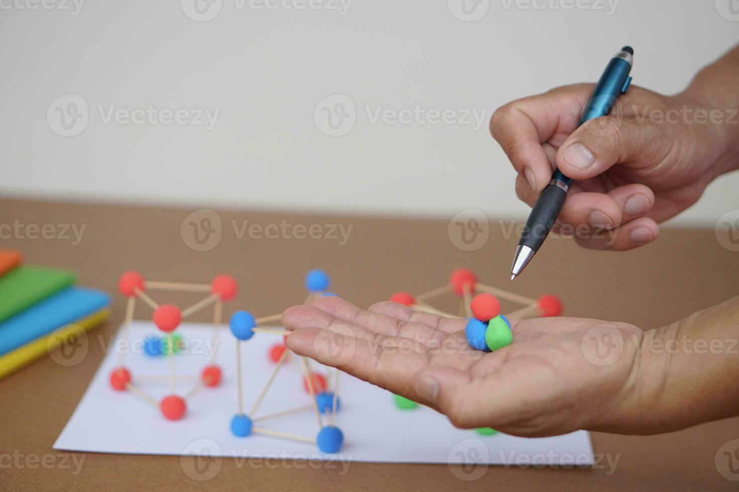 Close up teacher hands holds pen and plasticine balls to teach about basic molecule structure in chemist lesson. Concept, science education. Describing and analyzing. photo
