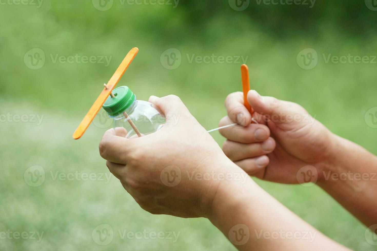 Close up hands hold DIY toy made from plastic bottle, rope and ice cream stick. Concept, Recycle crafts. Toy for kids, Teaching aid, fun activity for active learning. Spin for movement. DIY helicopter photo