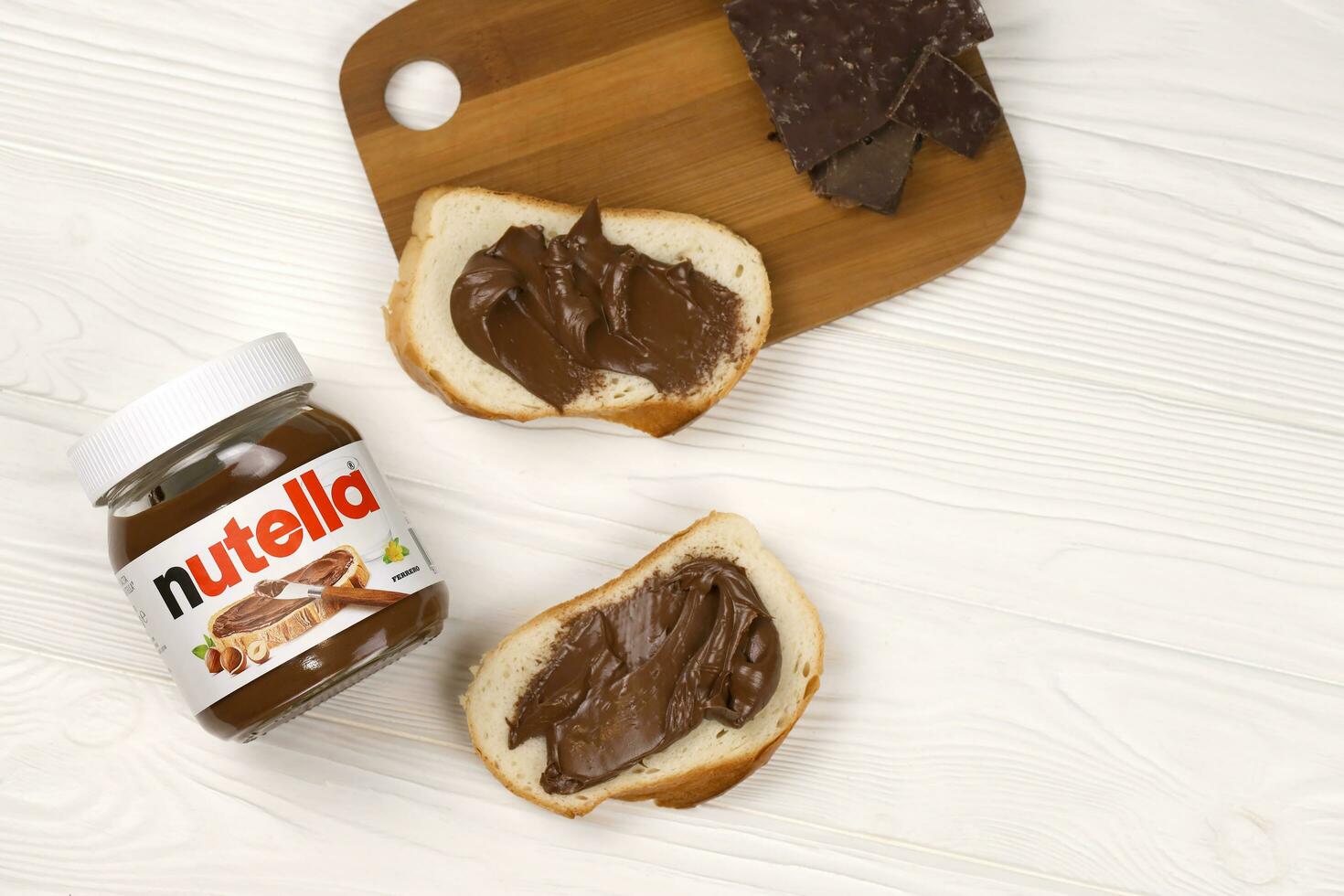 KHARKOV, UKRAINE - DECEMBER 27, 2020 Nutella glass can and spread on freshly baked bread. Nutella is manufactured by Italian company Ferrero first introduced in 1964 photo