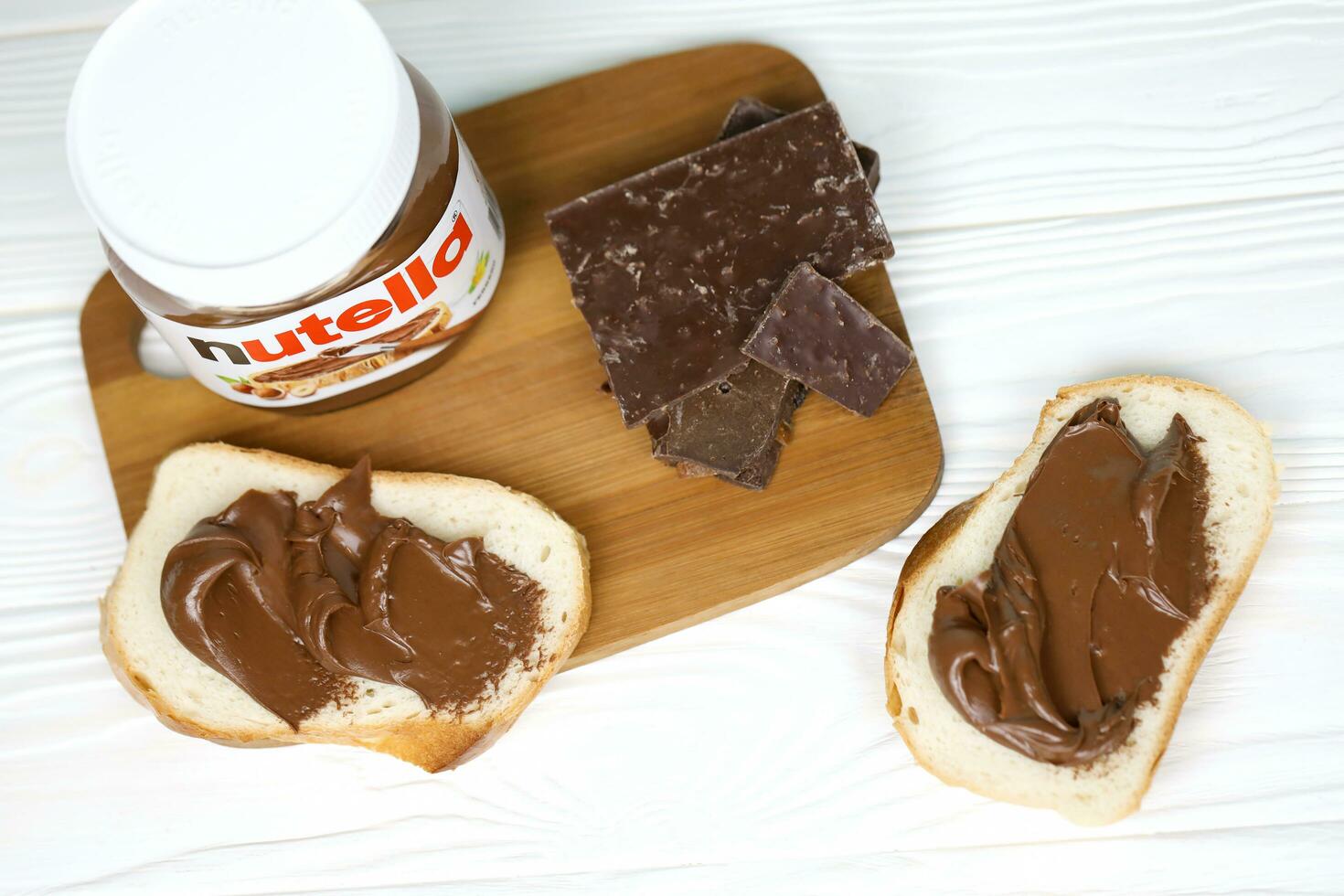 KHARKOV, UKRAINE - DECEMBER 27, 2020 Nutella glass can and spread on freshly baked bread. Nutella is manufactured by Italian company Ferrero first introduced in 1964 photo