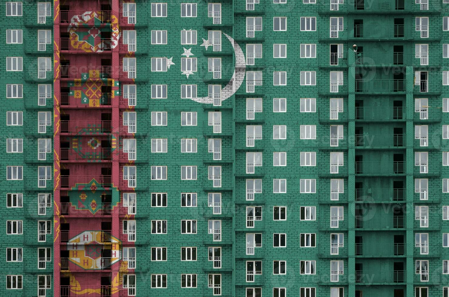 Turkmenistan flag depicted in paint colors on multi-storey residental building under construction. Textured banner on brick wall background photo