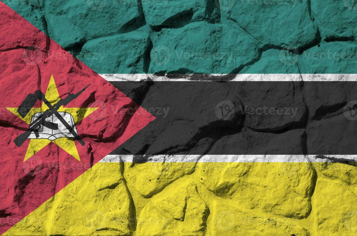 Mozambique flag depicted in paint colors on old stone wall closeup. Textured banner on rock wall background photo