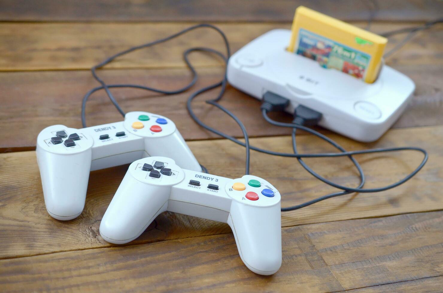 Old 8-bit video game console with game cartridge and two gaming joysticks on wooden background photo