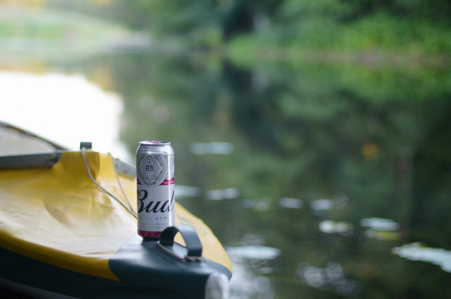 Budweiser Bud beer can on yellow kayak outdoors in the river and green trees blurred background photo