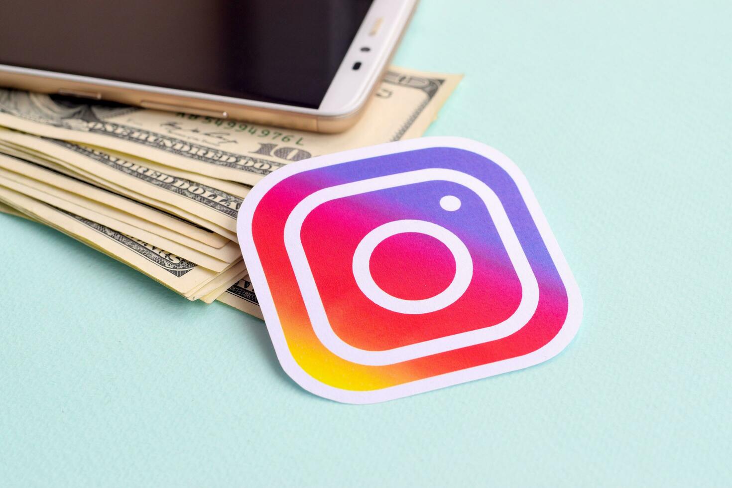 Instagram paper logo lies with envelope full of dollar bills and smartphone photo