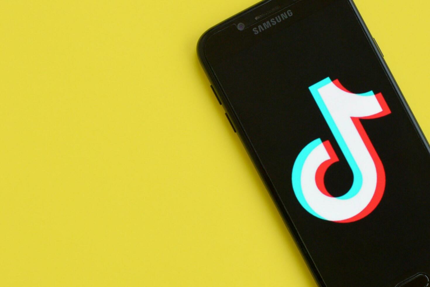 Tiktok logo on samsung smartphone screen on yellow background. TikTok is a popular video-sharing social networking service owned by ByteDance photo