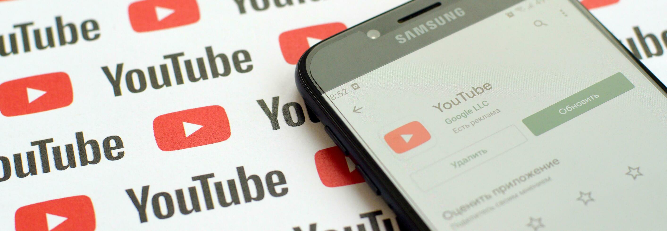 Youtube app on samsung smartphone screen on paper banner with small youtube logos and inscriptions. YouTube is Google subsidiary and American most popular video-sharing platform photo