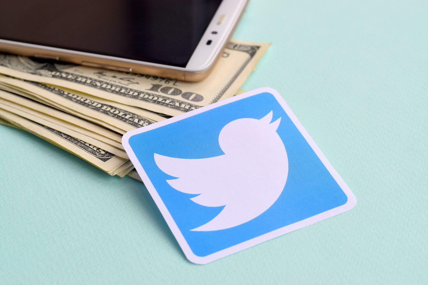 Twitter paper logo lies with envelope full of dollar bills and smartphone photo