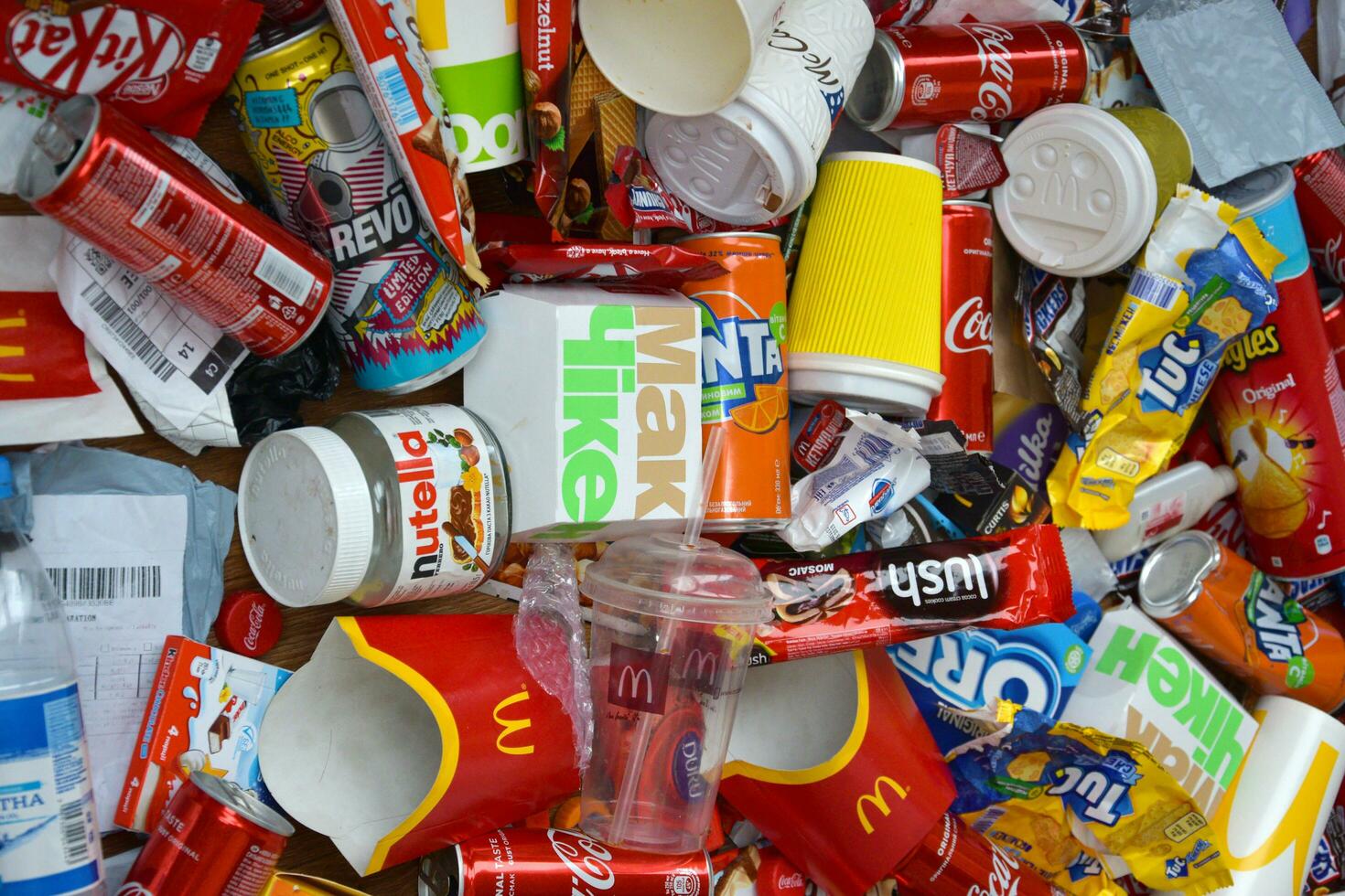 Big pile of many disposable colored trash from edible products of famous food and beverage manufacturers. Soda cans and chocolate bar wrappings in stack photo