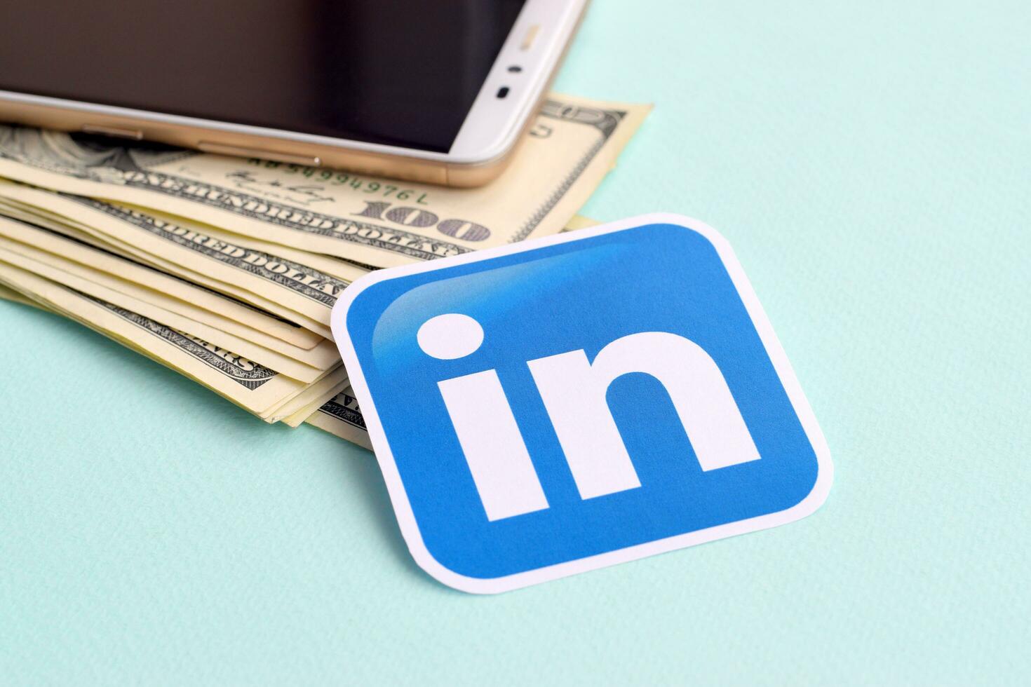 Linkedin paper logo lies with envelope full of dollar bills and smartphone photo