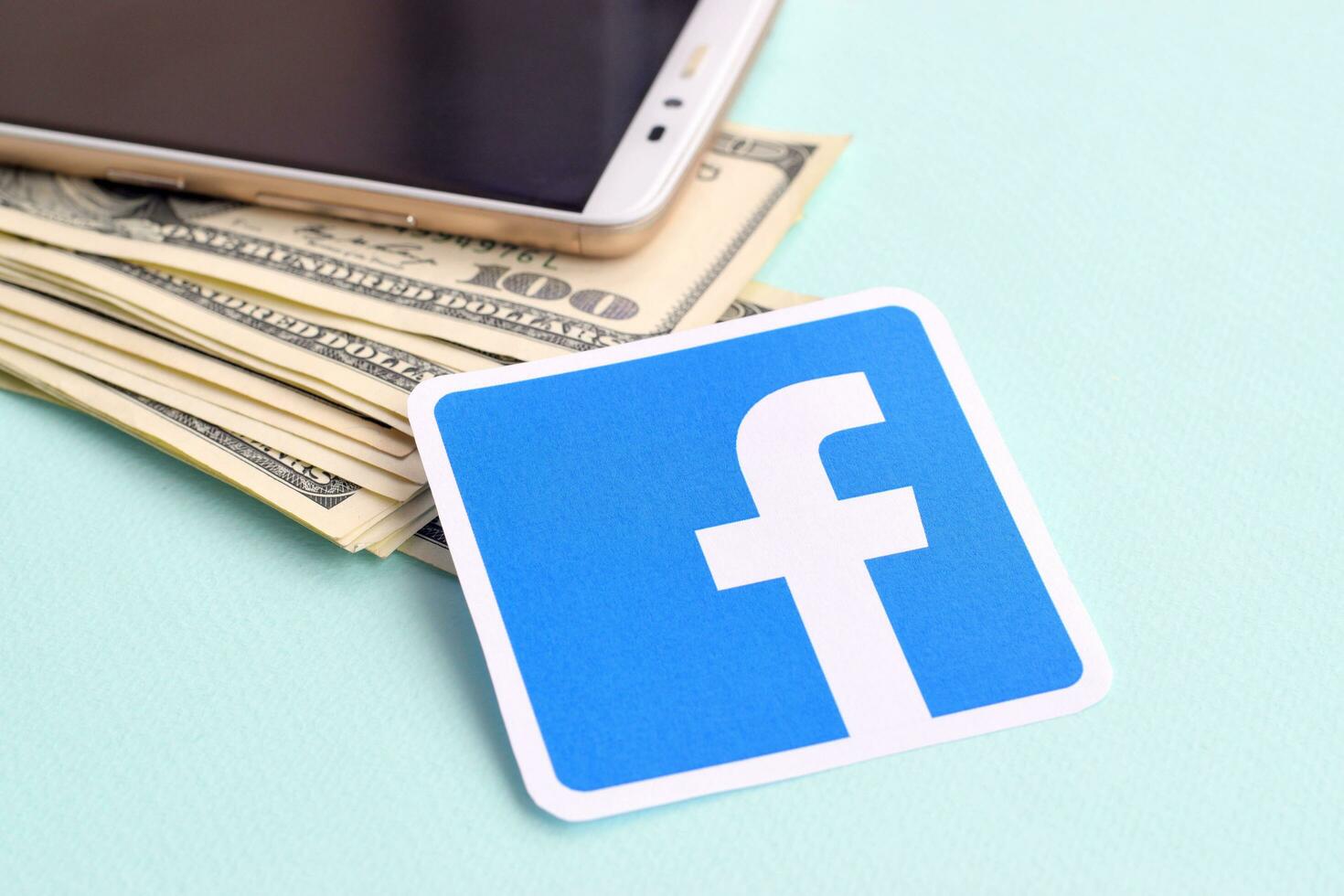 Facebook paper logo lies with envelope full of dollar bills and smartphone photo