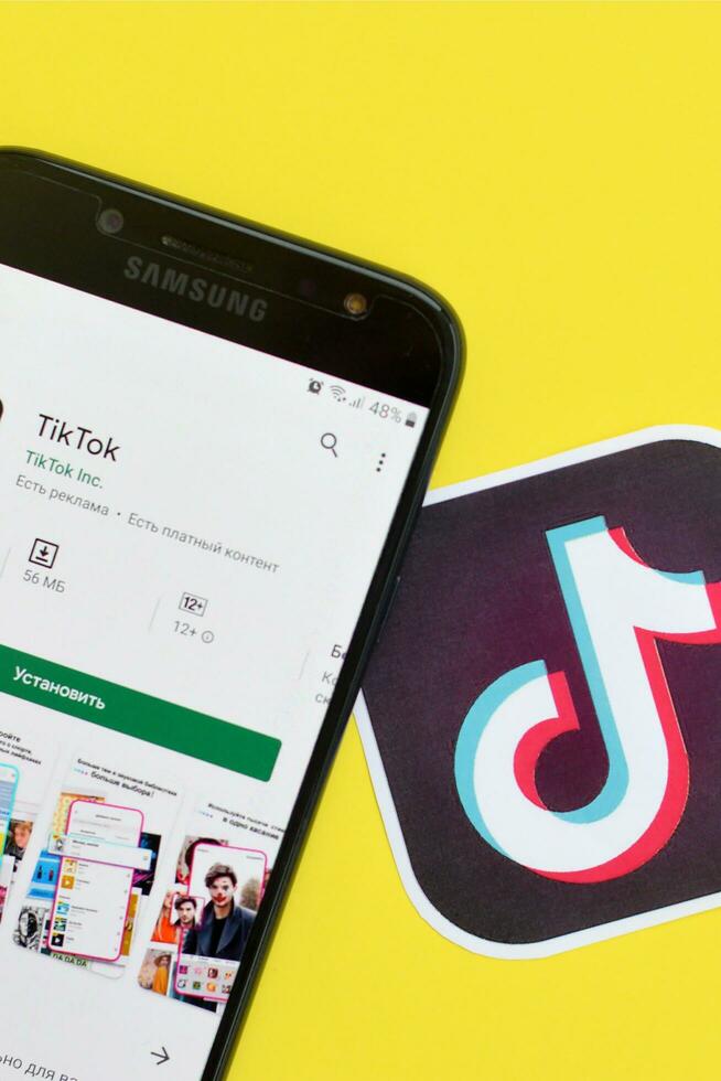 Tiktok application in playmarket on samsung smartphone screen on yellow background. TikTok is a popular video-sharing social networking service owned by ByteDance photo