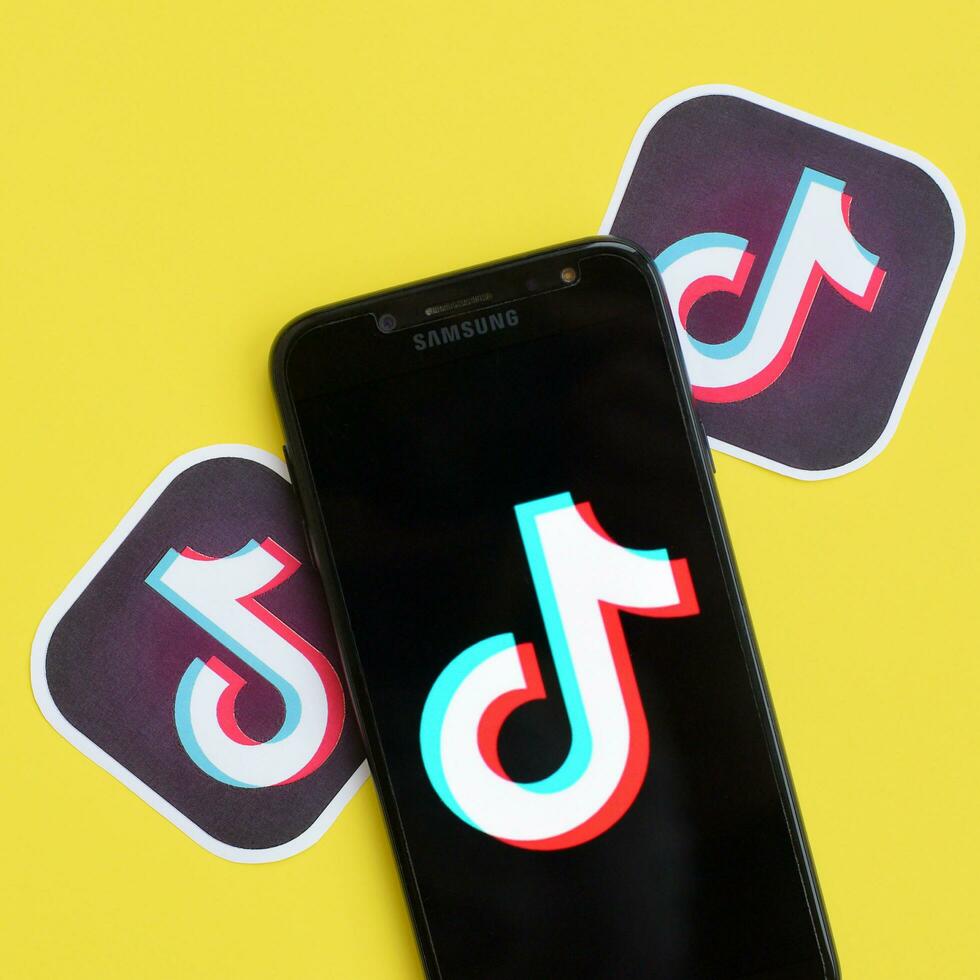 Tiktok logo on samsung smartphone screen on yellow background. TikTok is a popular video-sharing social networking service owned by ByteDance photo