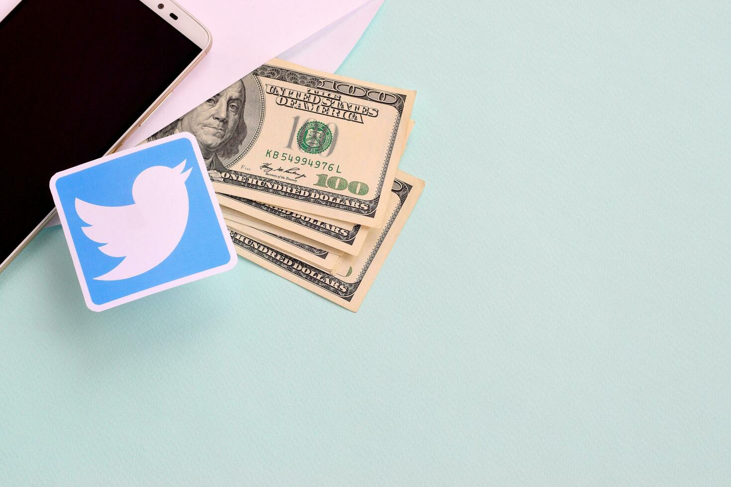 Twitter paper logo lies with envelope full of dollar bills and smartphone photo