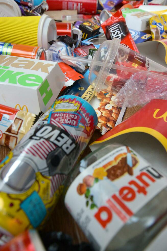Big pile of many disposable colored trash from edible products of famous food and beverage manufacturers. Soda cans and chocolate bar wrappings in stack photo