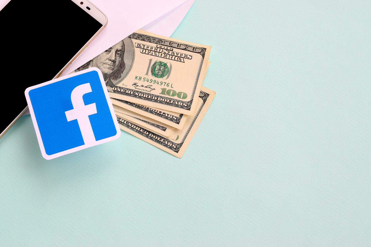 Facebook paper logo lies with envelope full of dollar bills and smartphone photo