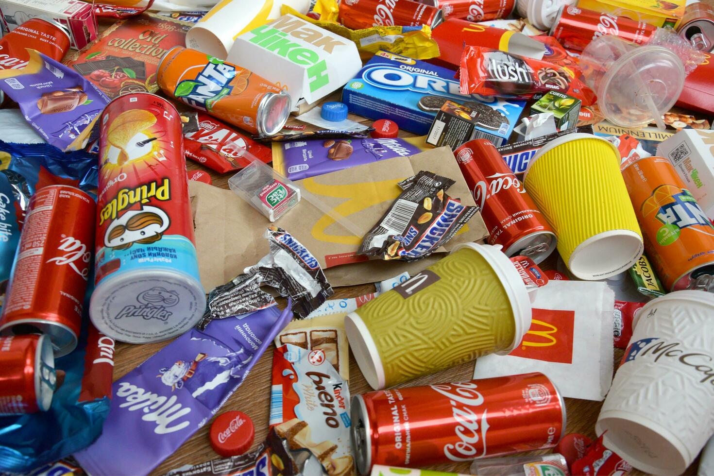 Big pile of many disposable colored trash from edible products of famous food and beverage manufacturers. Soda cans and chocolate bar wrappings in stack photo