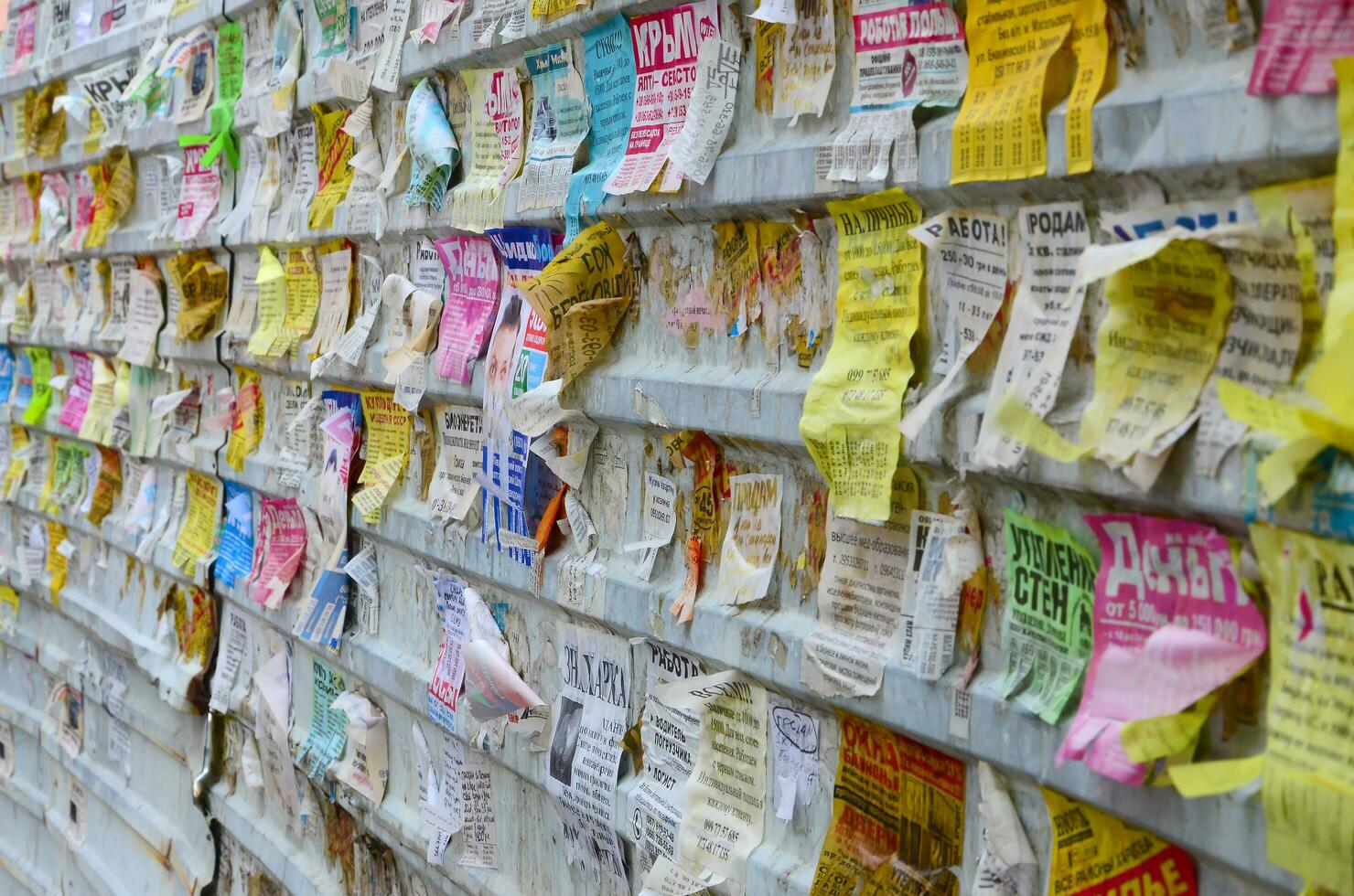 KHARKOV, UKRAINE - JUNE 24, 2018 Grunge Message Board with many advertisement. People spreading advertising and information on white paper than post it on metal fence photo