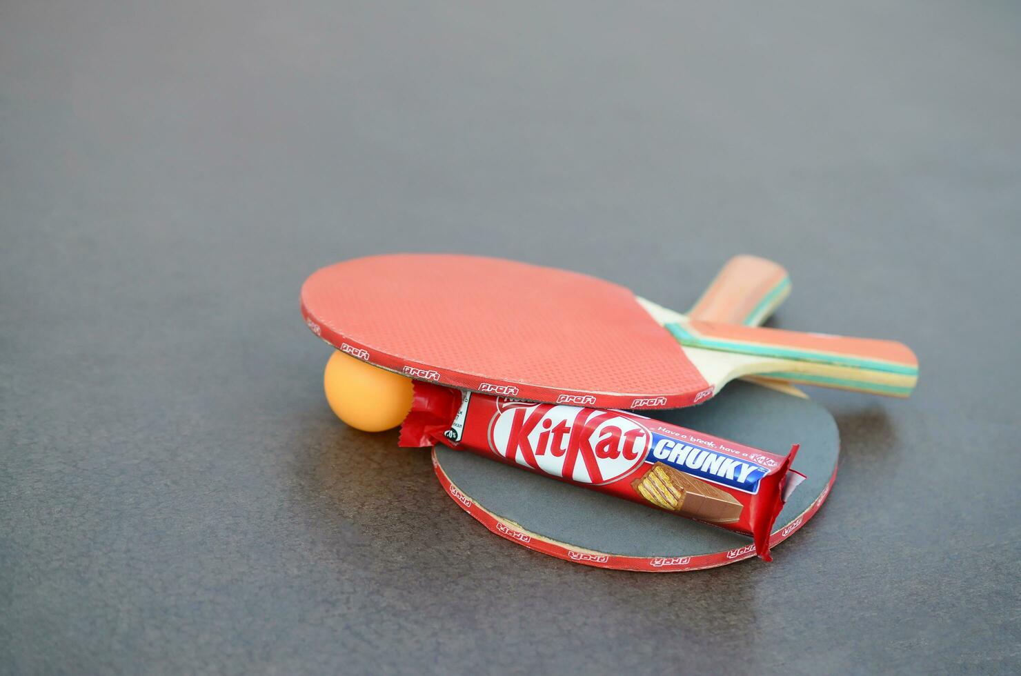 KHARKOV, UKRAINE - OCTOBER 17, 2019 Kit kat chocolate bar in red wrapping next to ping pong rackets and balls on table in a outdoor sport yard photo