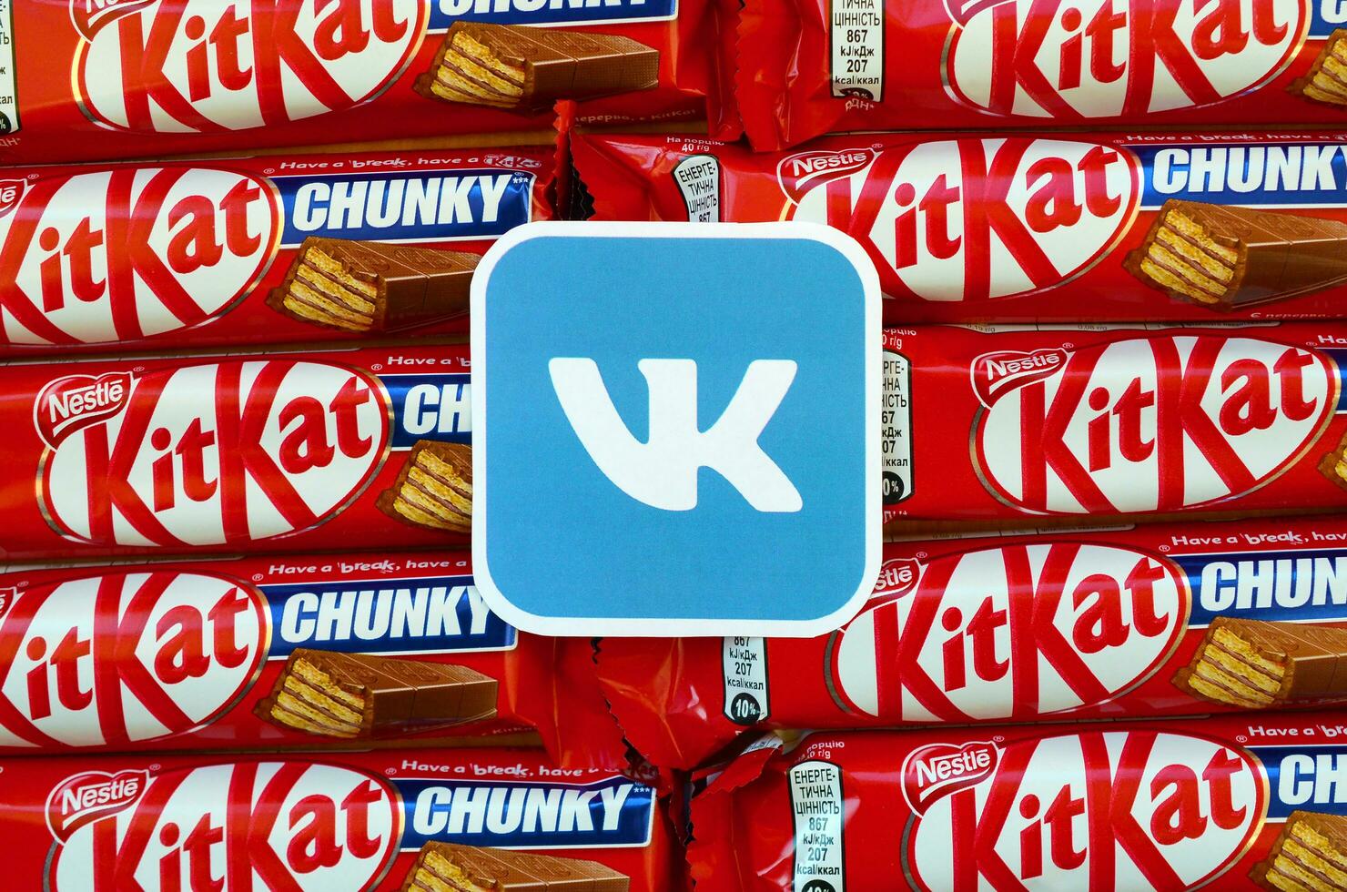 Vkontakte paper logo on many Kit Kat chocolate covered wafer bars in red wrapping. Advertising chocolate product in Vkontakte social network and world wide web photo