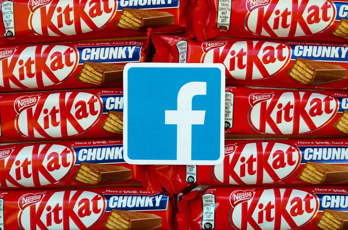 Facebook paper logo on many Kit Kat chocolate covered wafer bars in red wrapping. Advertising chocolate product in Facebook social network and world wide web photo