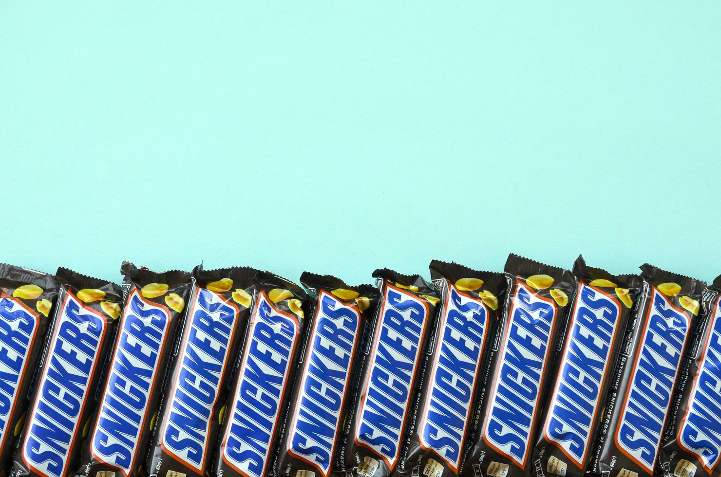 Many Snickers chocolate bars lies on pastel blue paper. Snickers bars are produced by Mars Incorporated. Snickers was created by Franklin Clarence Mars in 1930 photo