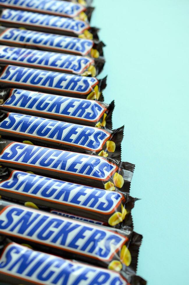 Many Snickers chocolate bars lies on pastel blue paper. Snickers bars are produced by Mars Incorporated. Snickers was created by Franklin Clarence Mars in 1930 photo