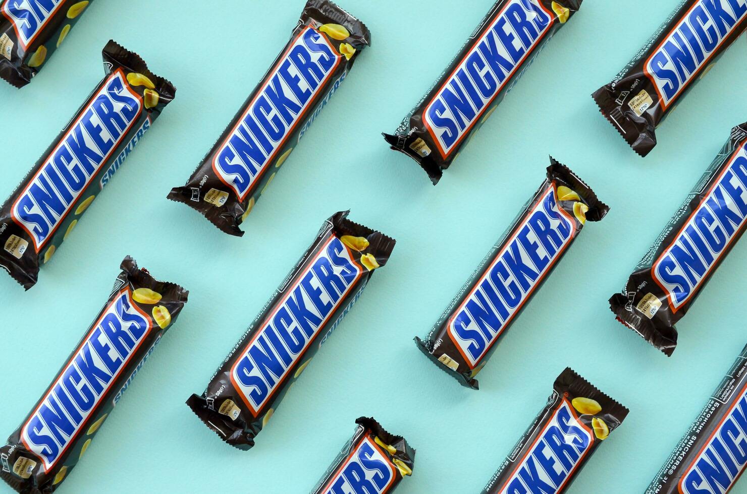 Many Snickers chocolate bars lies on pastel blue paper. Snickers bars are produced by Mars Incorporated. Snickers was created by Franklin Clarence Mars in 1930 photo