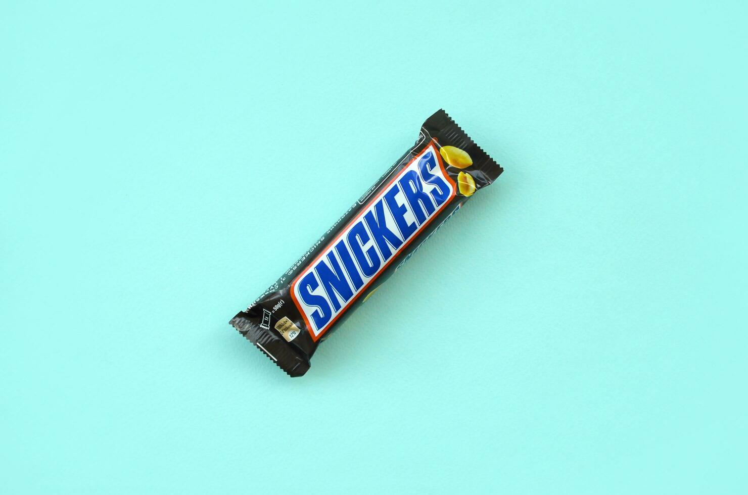 Many Snickers chocolate bars lies on pastel blue paper. Snickers bars are produced by Mars Incorporated. Snickers was created by Franklin Clarence Mars in 1930 photo