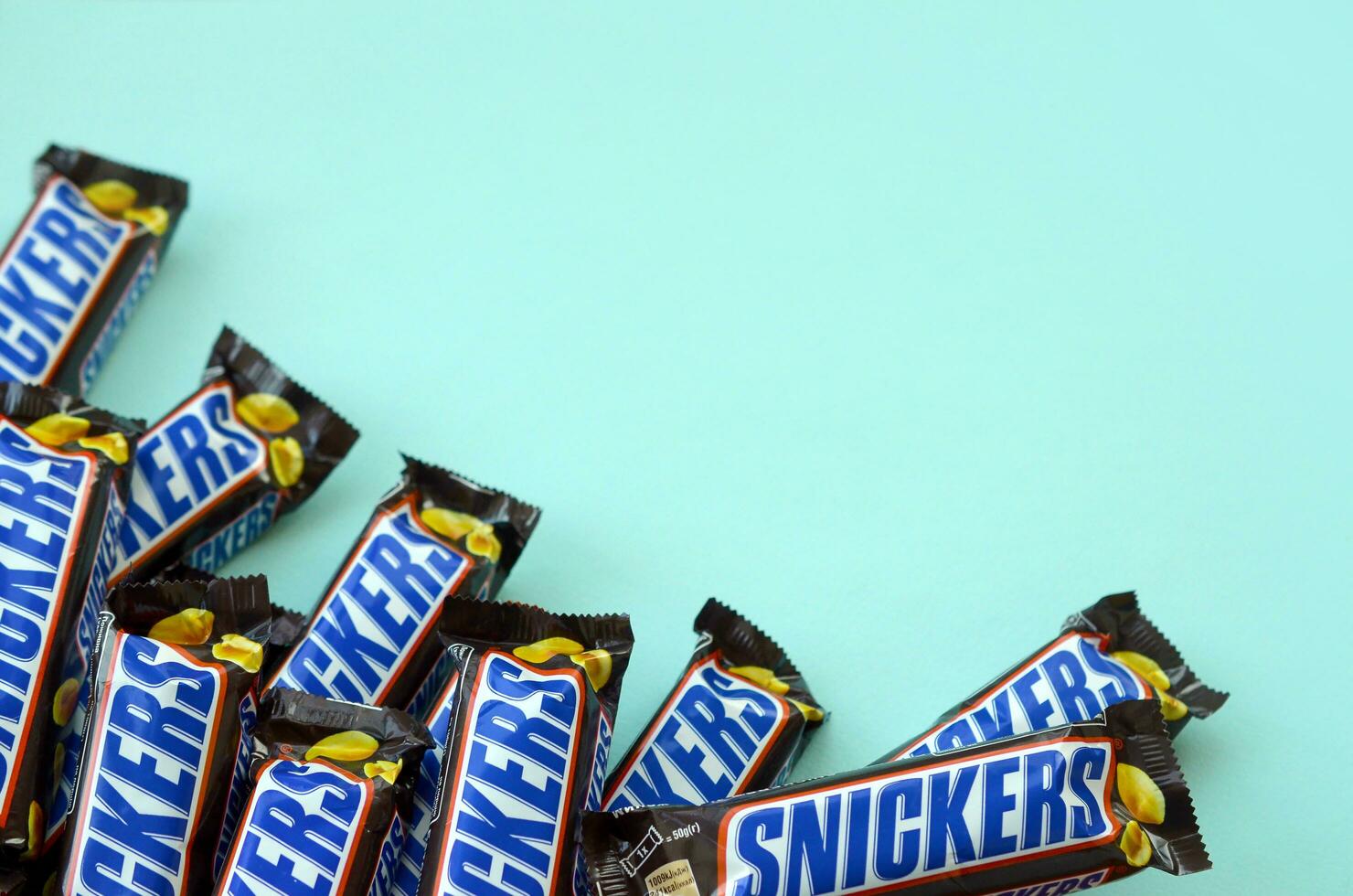 Many Snickers chocolate bars lies on pastel blue paper. Snickers bars are produced by Mars Incorporated. Snickers was created by Franklin Clarence Mars in 1930 photo