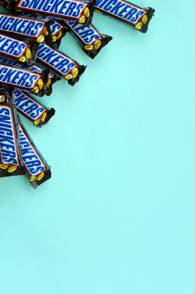 Many Snickers chocolate bars lies on pastel blue paper. Snickers bars are produced by Mars Incorporated. Snickers was created by Franklin Clarence Mars in 1930 photo