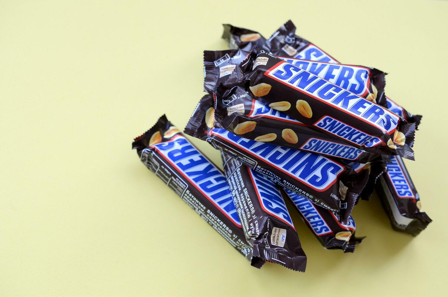 Many Snickers chocolate bars lies on pastel yellow paper. Snickers bars are produced by Mars Incorporated. Snickers was created by Franklin Clarence Mars in 1930 photo