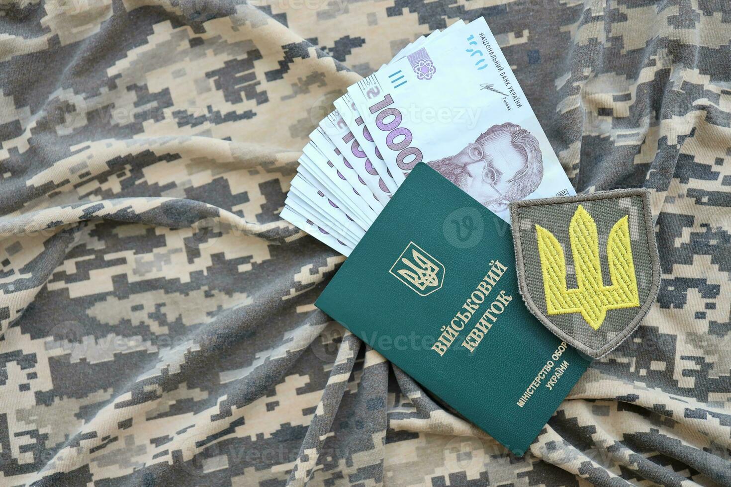 Symbol of Ukrainian army and military ID with bunch of money on the camouflage uniform of a Ukrainian soldier. Concept of payment to military personnel or bribe for deferment from service photo