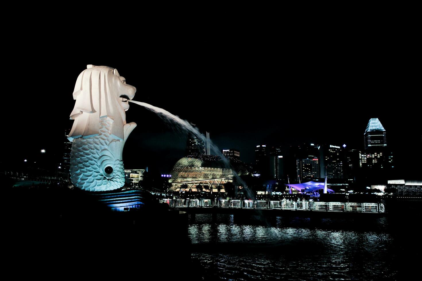 Singapore, August 20, 2023- Side view of Merlion spraying the water with cityscape at night and lake in background photo