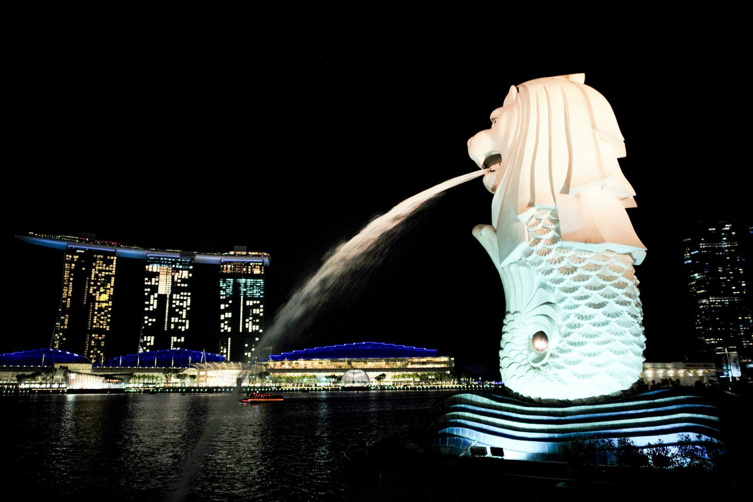 Singapore,August 20, 2023 Side view of Merlion spraying the water with cityscape at night and lake in background photo