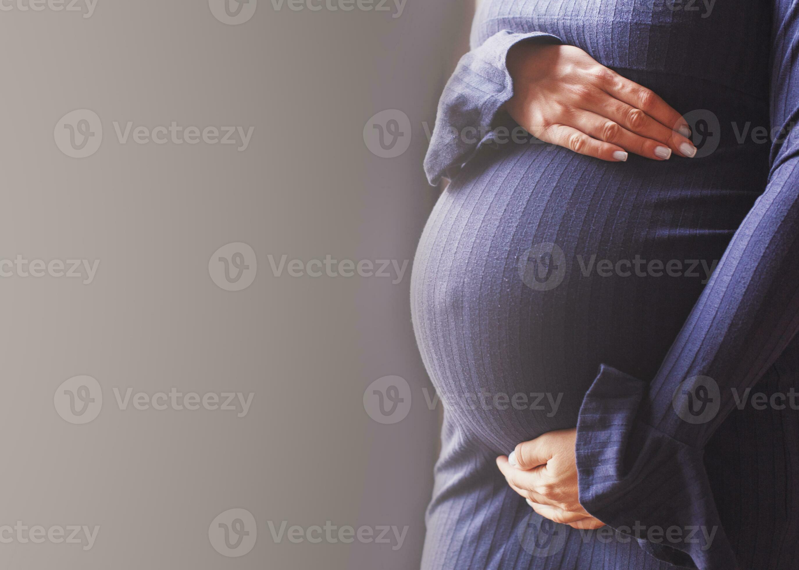 pregnant woman's belly closeup. hands hugging belly in blue background