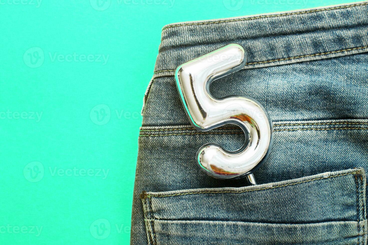 number 5 sticking out of the back pocket of blue jeans on green background photo
