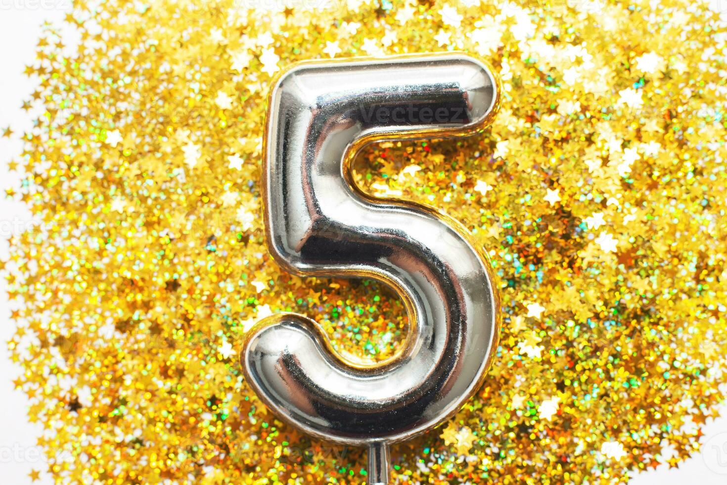 Five years birthday party. number five with golden confetti in form of stars on yellow background photo