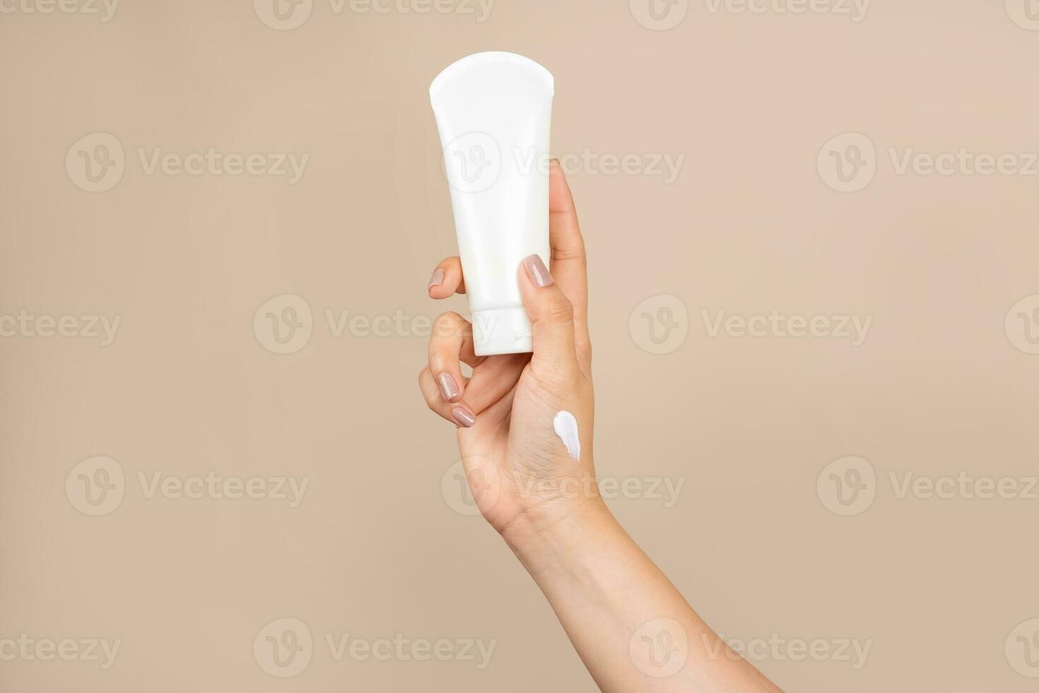 Female hand with cream to touch cosmetic tube on beige background. Concept of hand lotion cream or winter facial care. photo