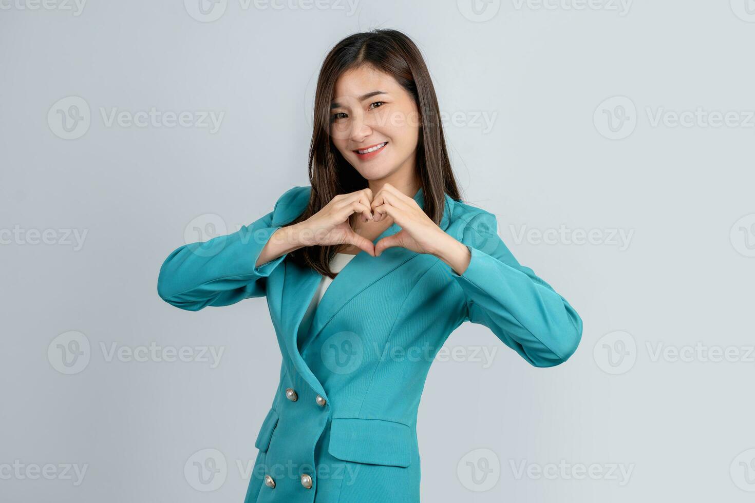 Happy asian business woman in bright green suit showing heart sign with hands isolated on white background photo