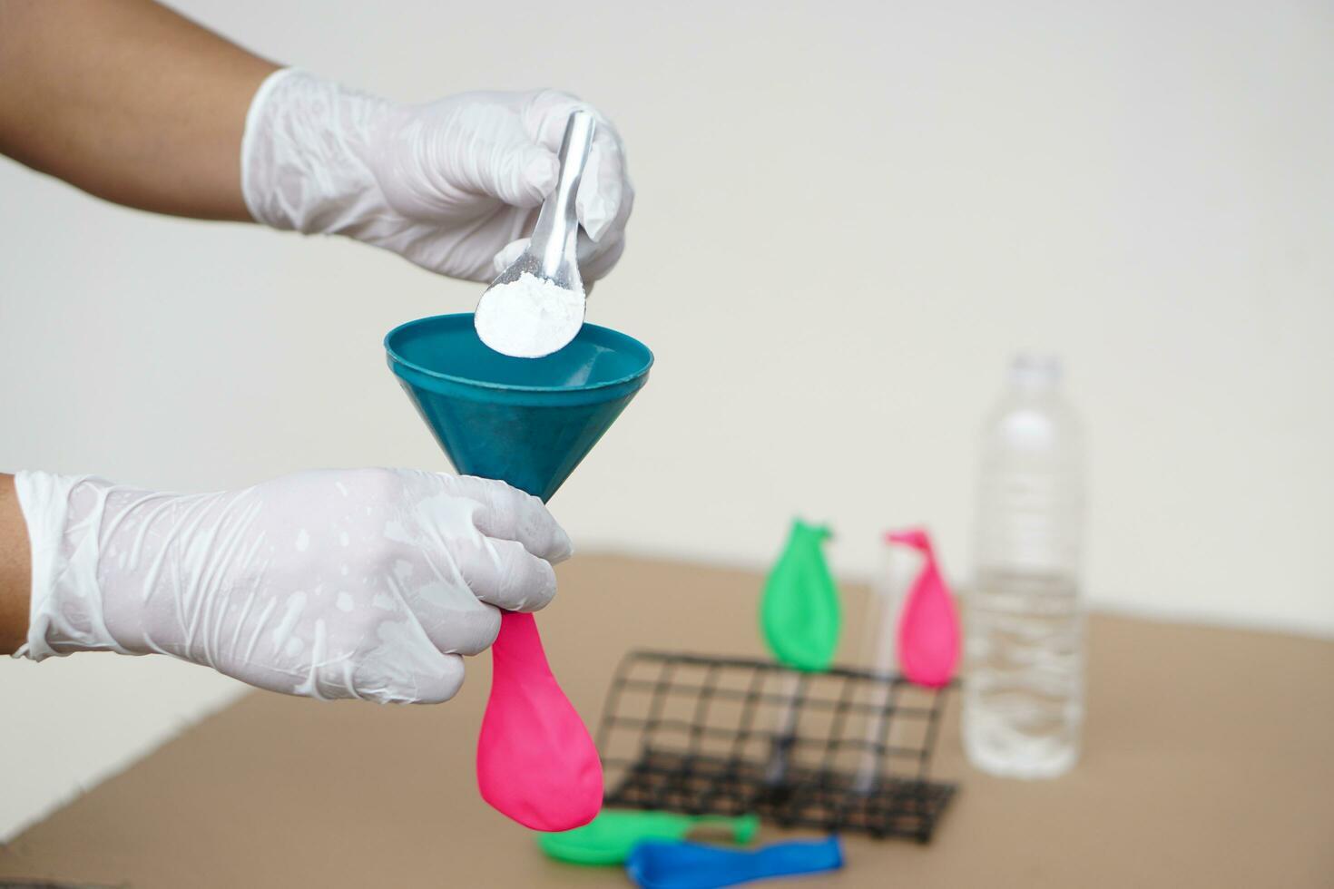 Closeup hands wears gloves holds funnel and flat pink balloon, put spoon of baking soda powder to pour into balloon. Concept, science experiment about reaction of chemical substance . photo