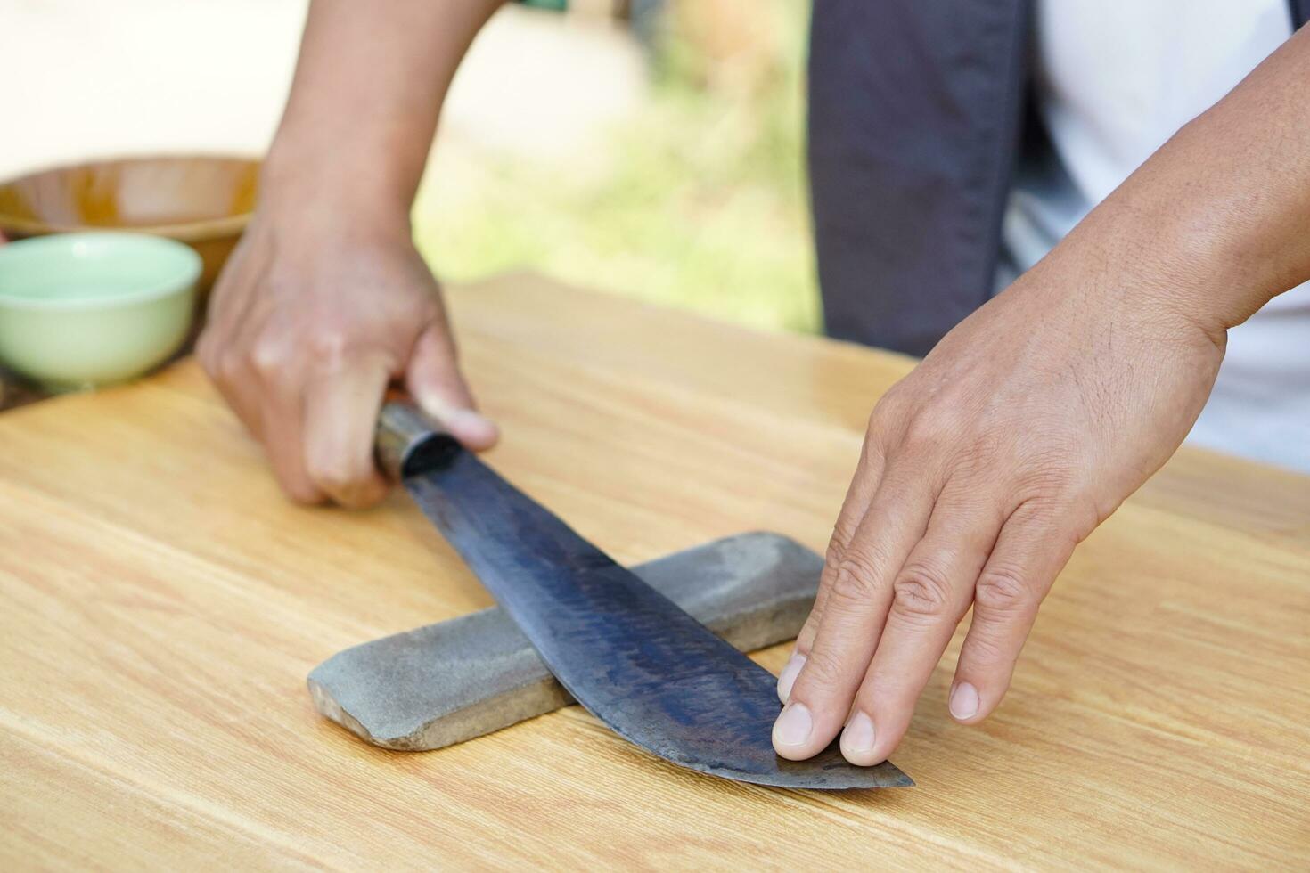 Closeup man hands sharpen knife on whetstone sharpener or grindstone. Concept, maintenance tools for cooking, make knife sharp ,not dull for long live using. Original style. photo