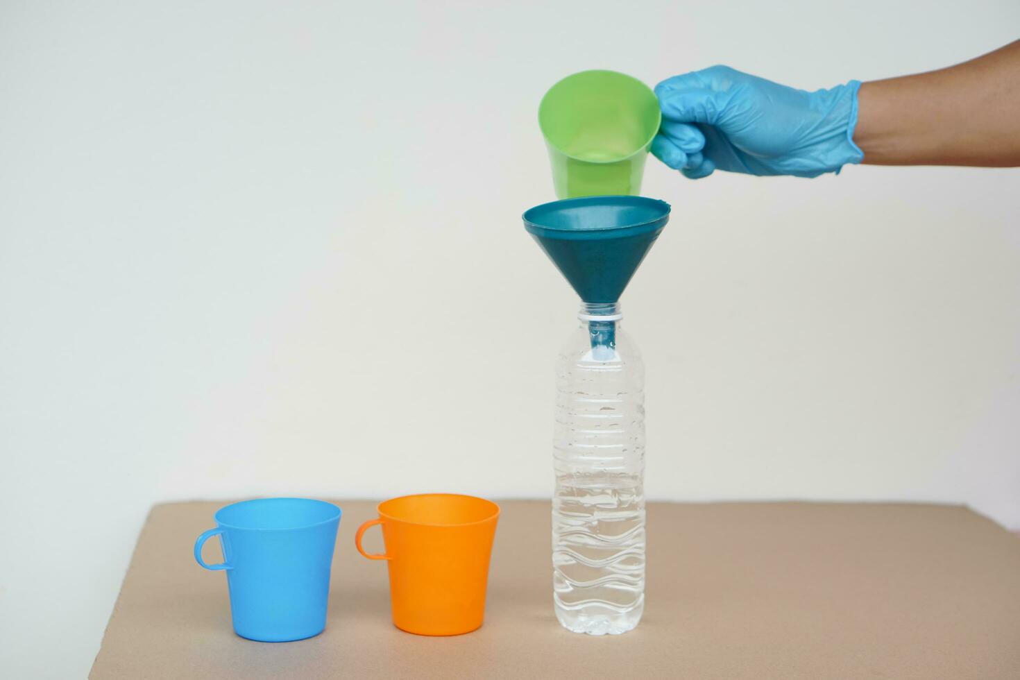 Closeup hand wear blue glove holds green mug to pour water into bottle to do science experiment. Concept, water quantity measurement for mixing chemical substances. photo