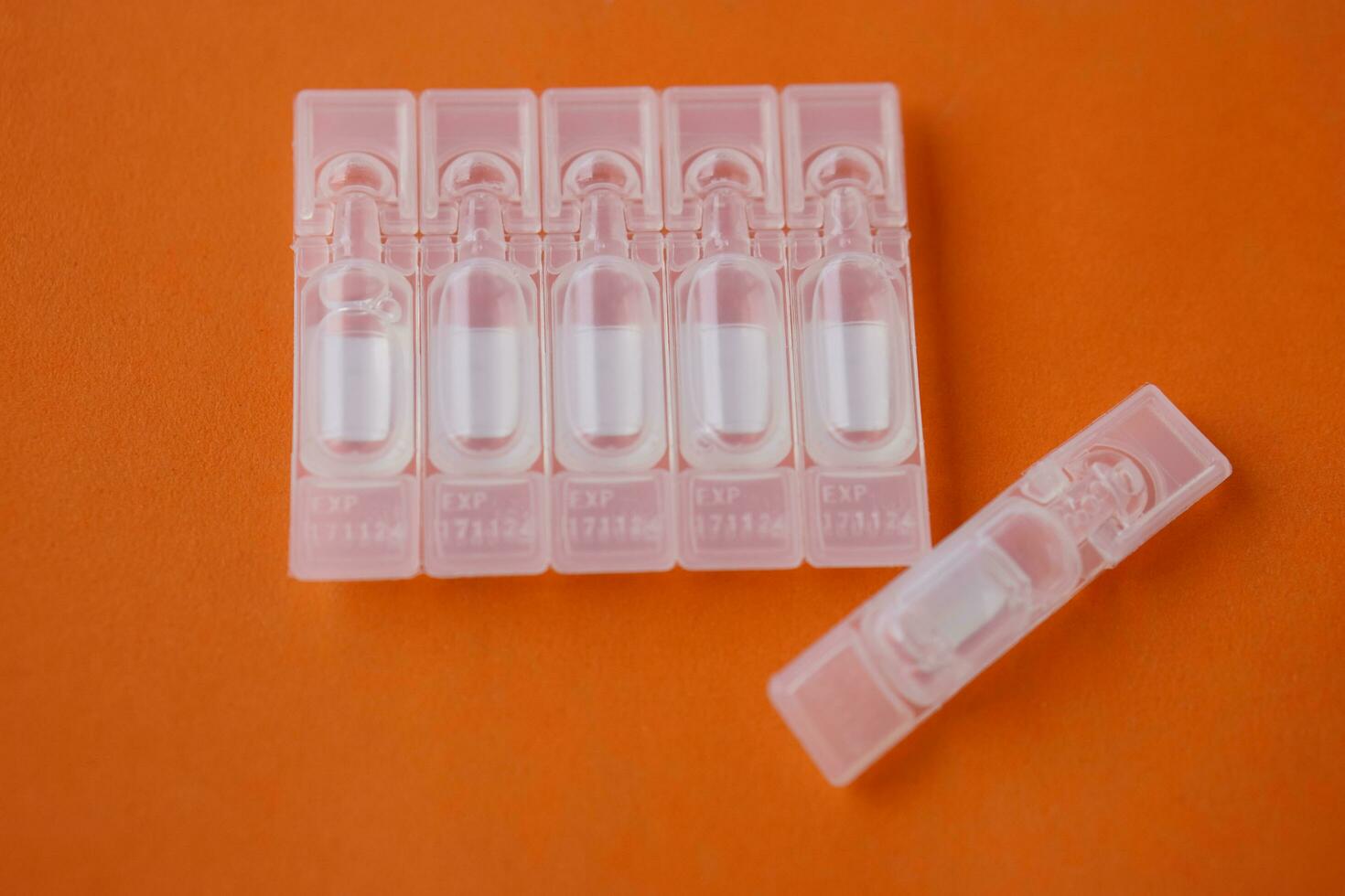 Single use artificial tear lubricant eye drops containers, tubes, isolated on orange background. Concept, medical products for dry eyes or eyes disease treatment. Use under doctor prescription. photo