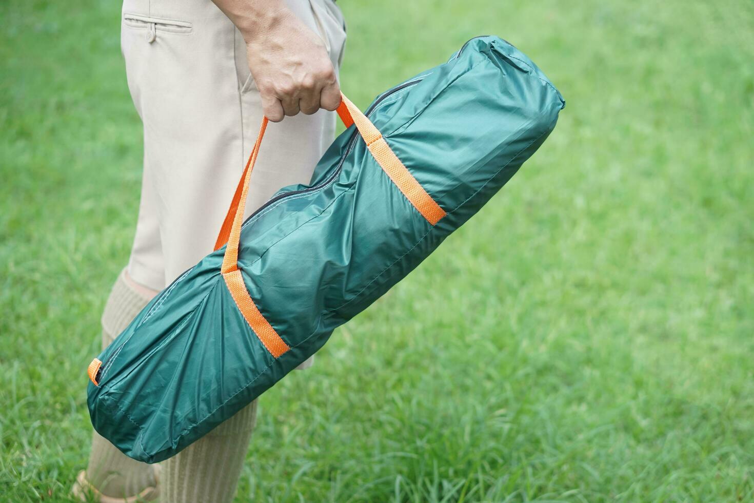 Close up man carry a green bag of tent to go camping outdoor. Concept, camping tent, equipment as accomodation for temporary outdoor sleeping as hiking or backpacking. photo