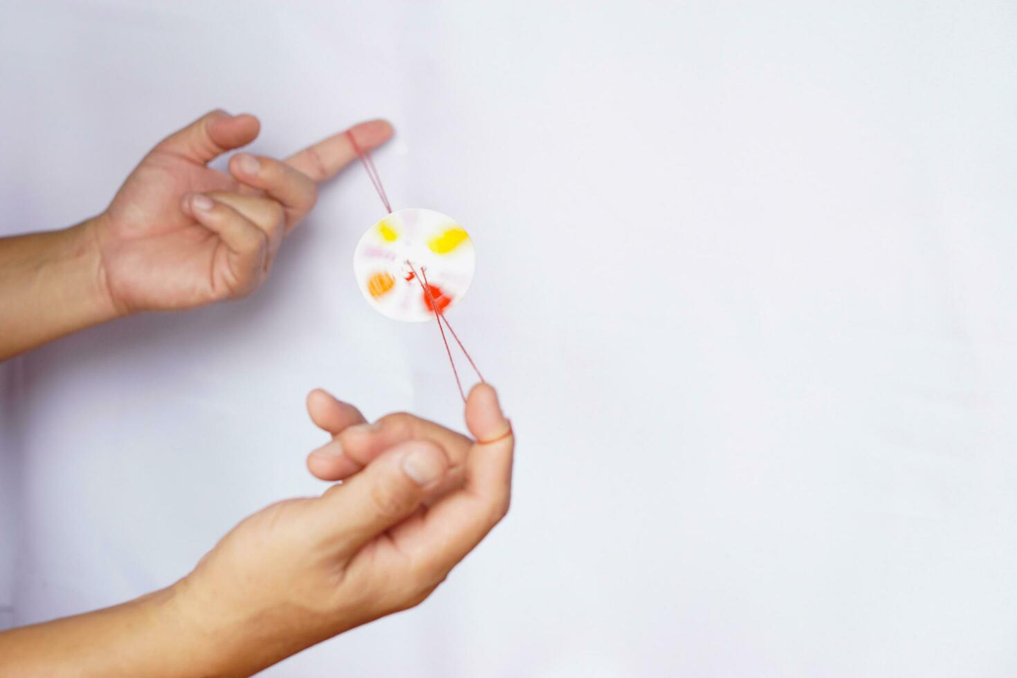 Hands are playing the diy spinning wheel toy, made from string and circle paper. Concept, retro toy which apply with science knowledge. Potential energy  in the rope when unwinding creates kinetic. photo