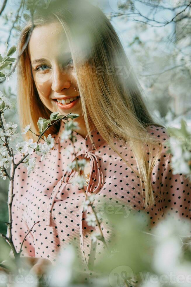 rubia niña en un primavera caminar en el jardín con Cereza flores hembra retrato, de cerca. un niña en un rosado polca punto vestido. foto