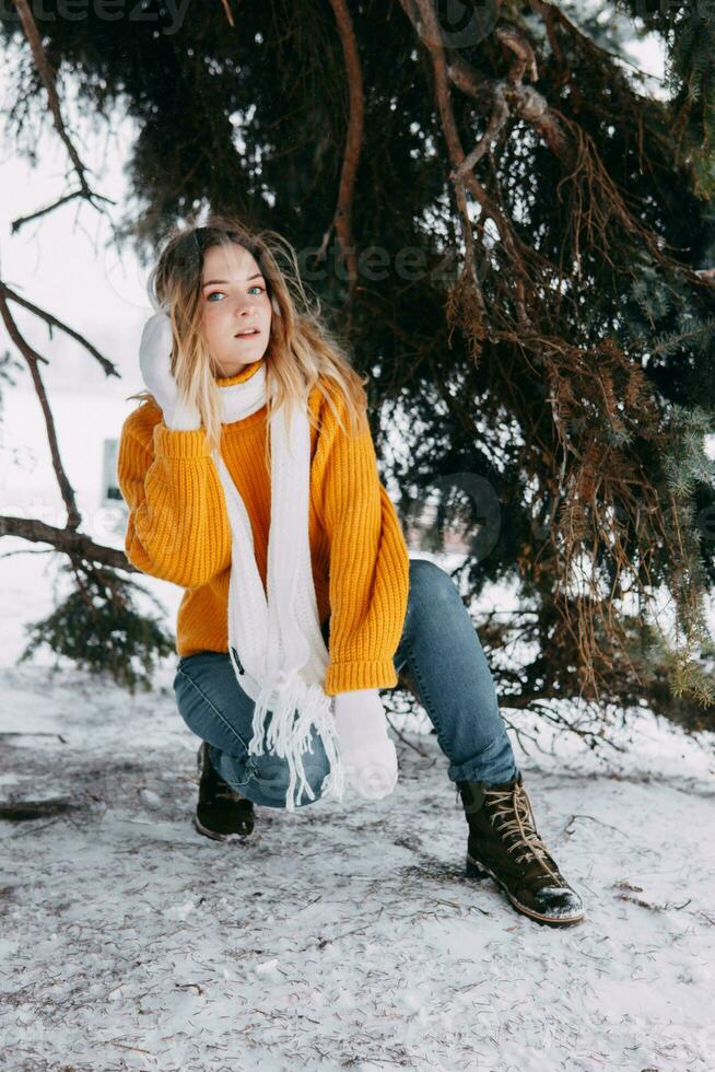 adolescente rubia en un amarillo suéter fuera de en invierno. un Adolescente niña en un caminar en invierno ropa en un Nevado bosque foto