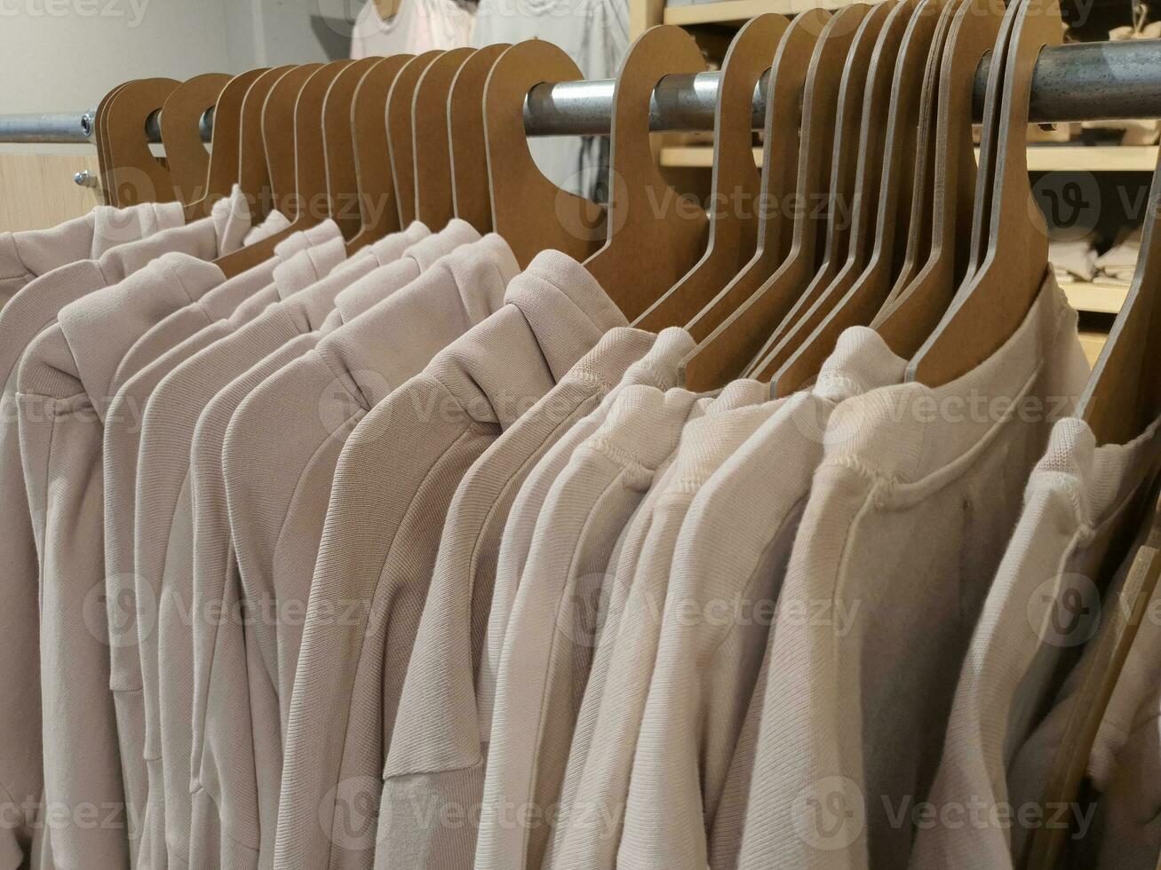 Casual clothes hang on ecofriendly cardboard paper hangers on rack in clothes store in trendy pastel tones and beige color. Gender free clothing concept. Selective focus photo