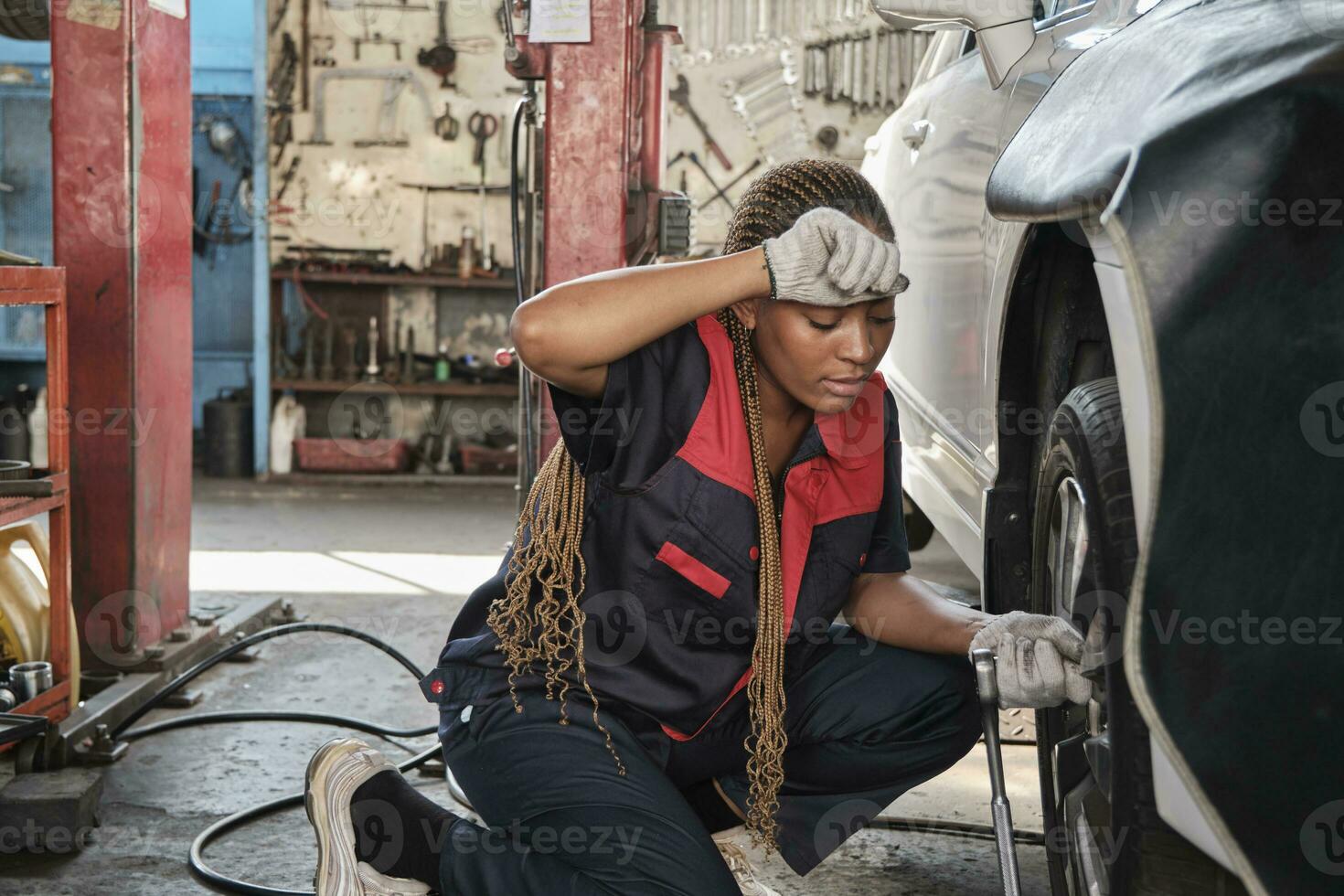 negro hembra automotor mecánico trabajador empulgueras coche rueda nueces con llave inglesa para reparar a cochera, toallitas apagado sudor, cansado con labor obras, vehículo mantenimiento Servicio trabajos, industria ocupación negocio. foto